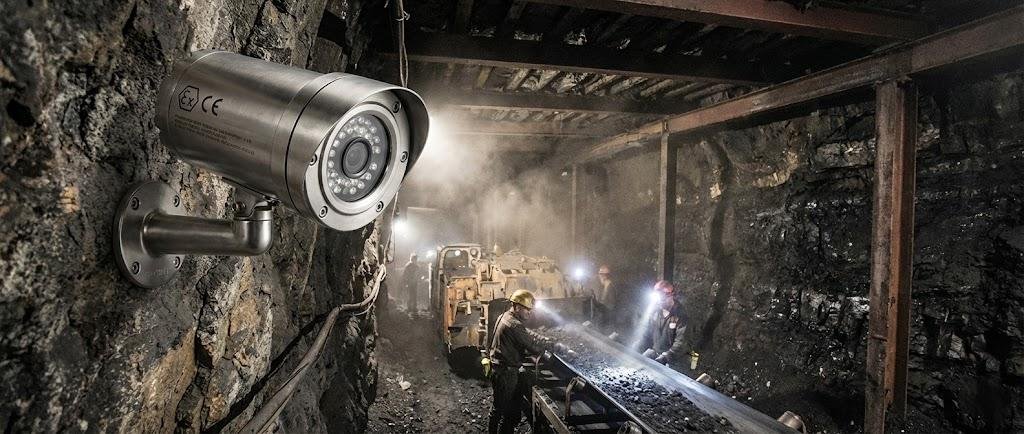 SWGJ stainless steel explosion-proof bullet camera mounted on an underground coal mine tunnel wall monitoring miners and conveyor belts.